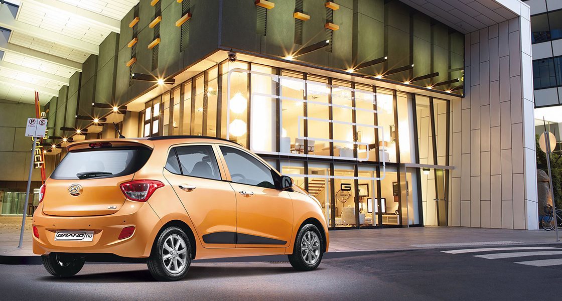 Side-front view of orange Grandi10 with lakeside view at night